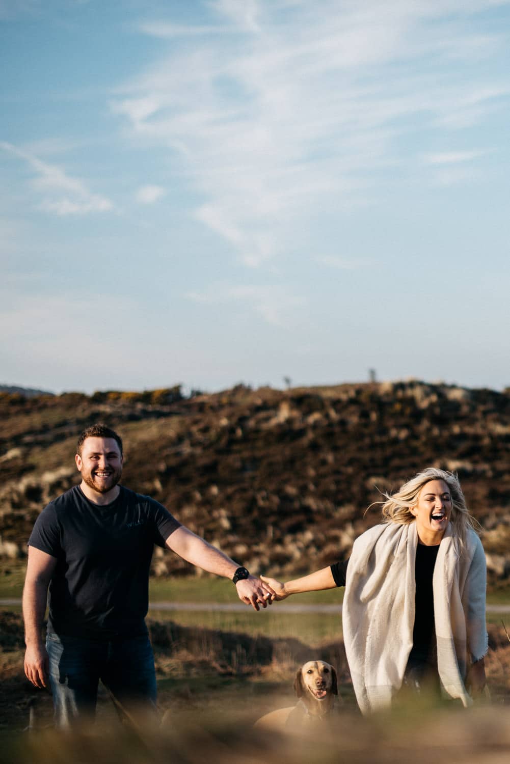 couple holding hands laughing with dog