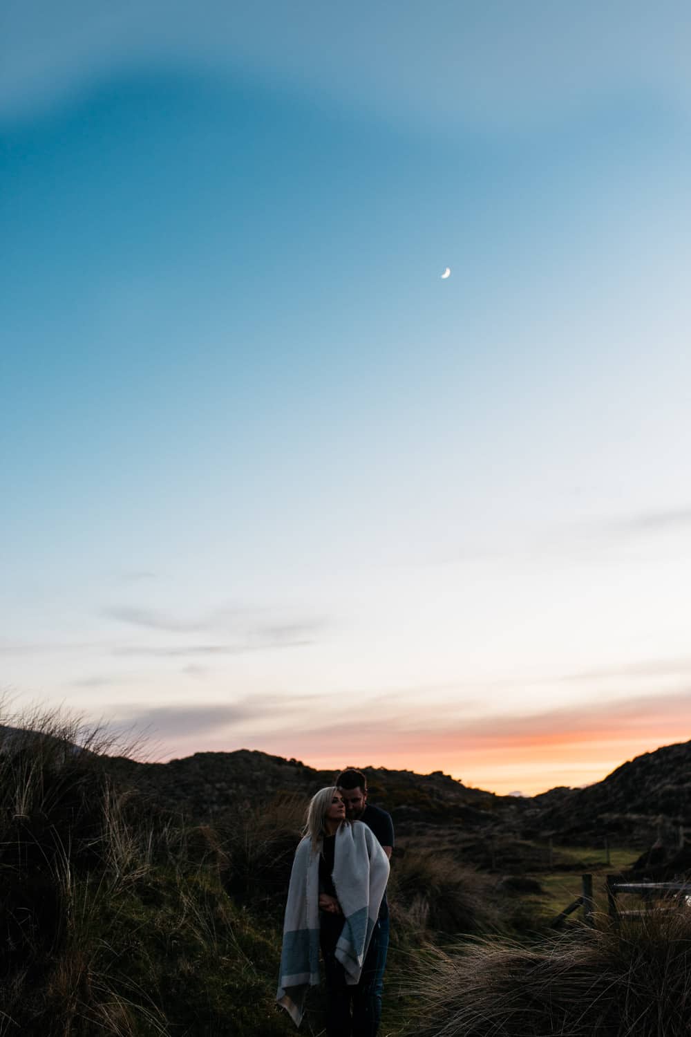 couple hugging at sunset with moon Engagement Photography Belfast