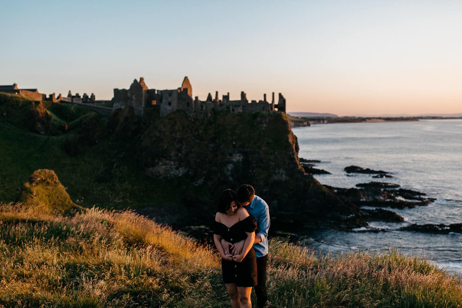 couple hugging in from of Dunluce Castle Engagement Photos Northern Ireland