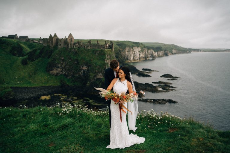 couple holding each other in front of Dunluce Castle Northern Ireland Elopement Photographer