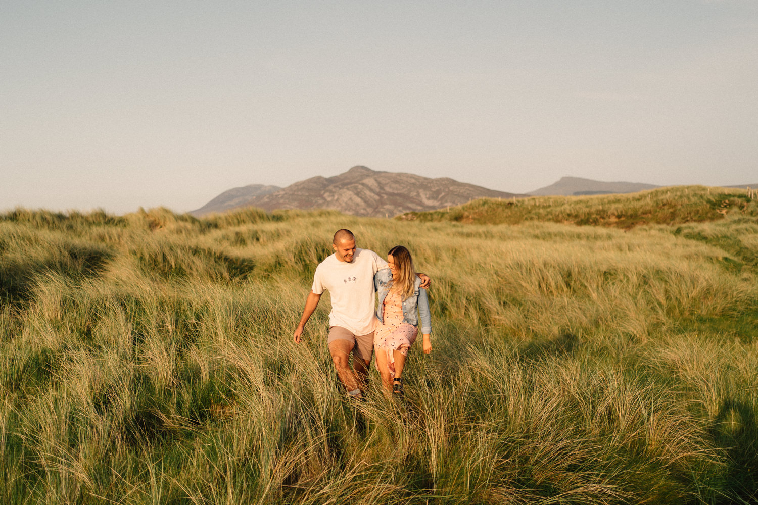 couple walking through the grass with mountains in the background on their engagement shoot Northern Ireland Wedding Photographer