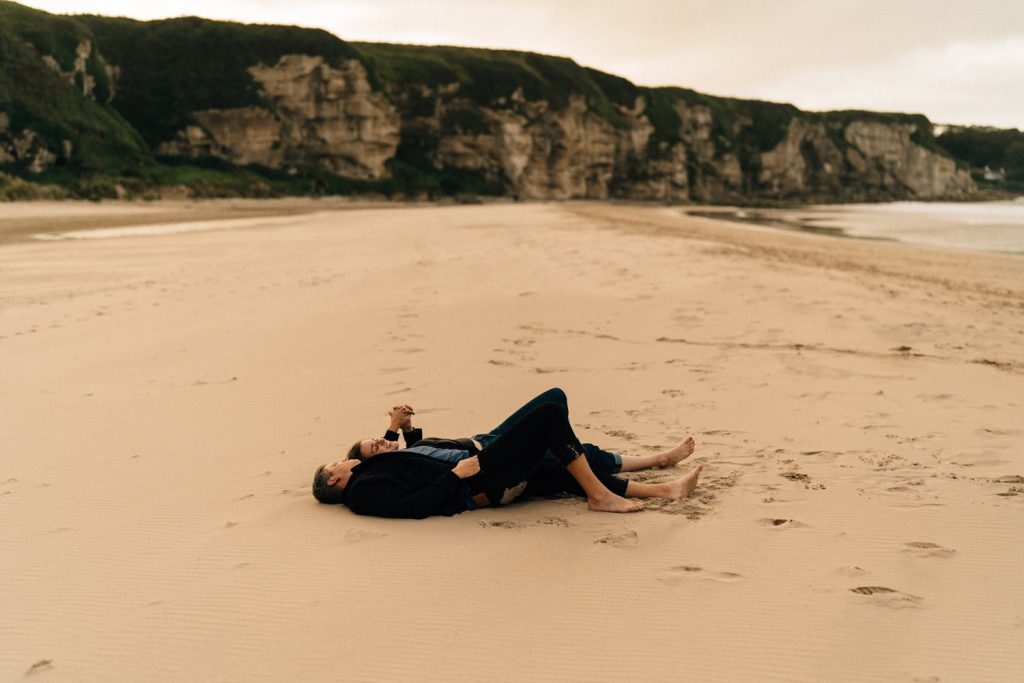 couple laying down on the sand at white park bay beach Elopement Photographer - Couples Photographer