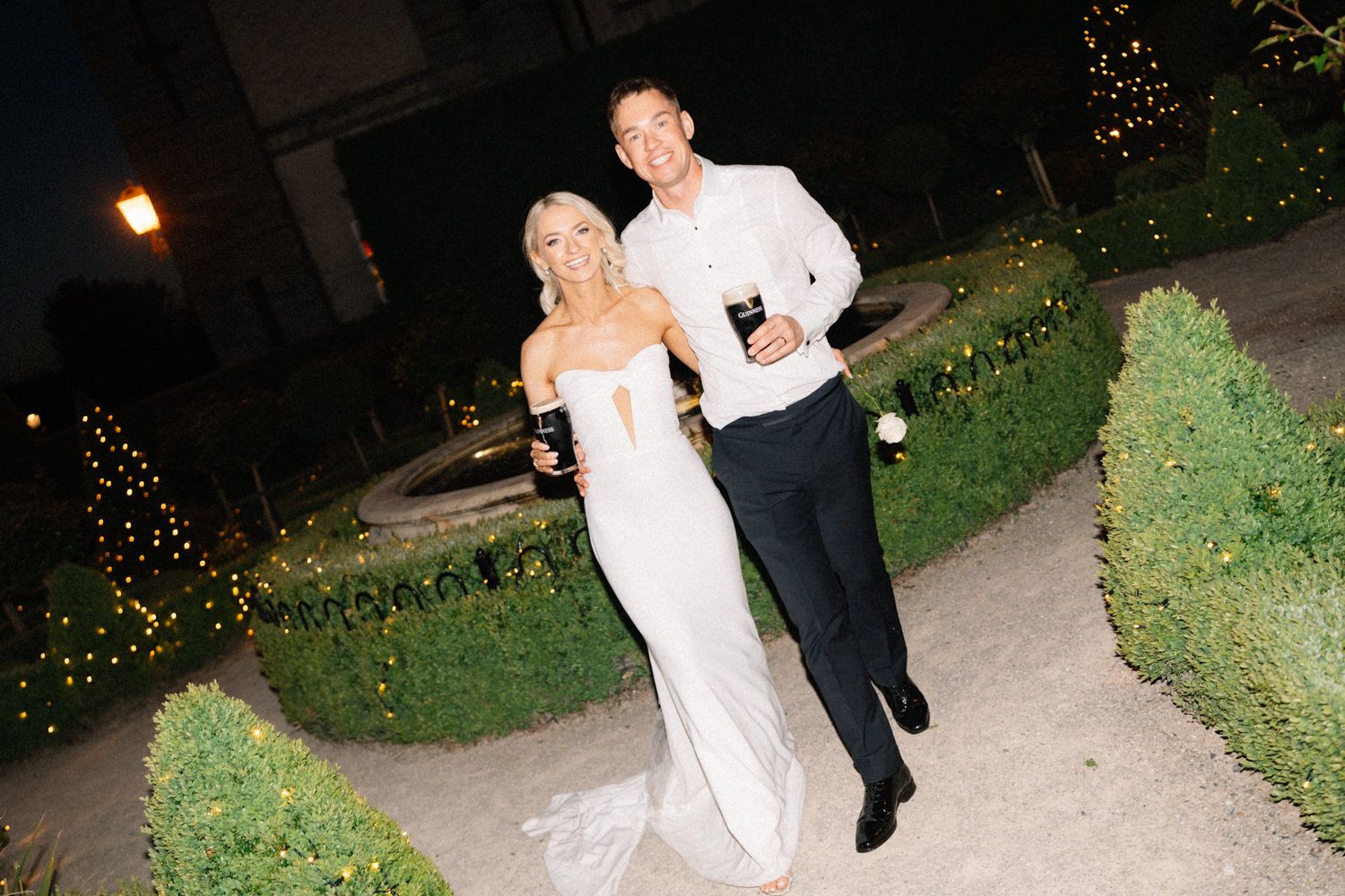 bride and groom walking in garden with Guinness Captured by a Cabra Castle Wedding Photographer